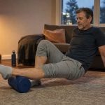 A runner using a foam roller on his calf on the living room floor after a run