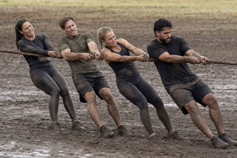 A team of obstacle racers hauling a heavy rope together through a muddy field