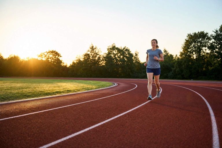 A woman running at an easy pace in the inside lane of an empty running track at sunrise