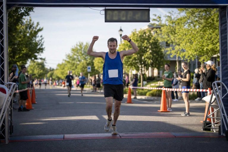 A runner crosses the finish line of a local 5K with the race clock overhead